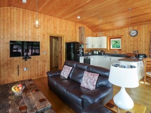 a living room with a leather couch and a kitchen at Barn Shelley Lodge in Copplestone