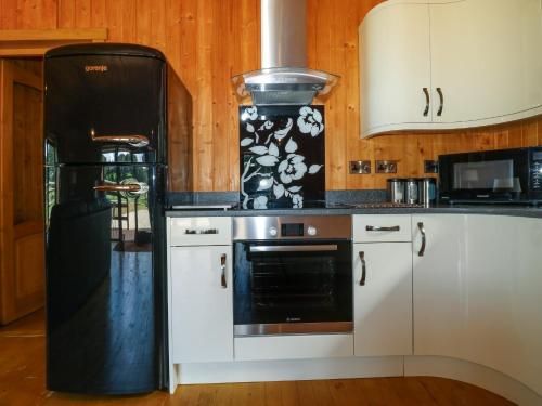 a kitchen with a black refrigerator and white cabinets at Barn Shelley Lodge in Copplestone