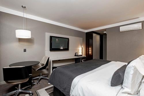 a hotel room with a bed and a desk and a tv at Full Jazz by Slaviero Hotéis in Curitiba