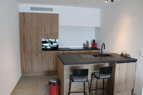a kitchen with a counter with two chairs and a sink at Ruim nieuwbouwappartement oostduinkerke in Oostduinkerke