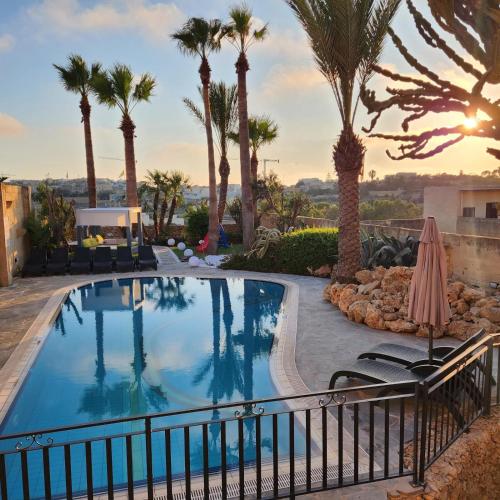 a swimming pool with palm trees and a resort at Il-Bejta Farmhouse in Għarb