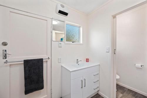 La salle de bains blanche est pourvue d'un lavabo et d'une douche. dans l'établissement Lakeside Escape - Motuoapa Holiday Home, à Turangi