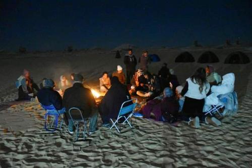 a group of people sitting around a fire on the beach at El Camel Hotel in Bawati