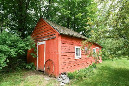 a red shed with a wheel in the grass at 1820 House - VT Charm + Modern Comforts + Hot Tub in Stowe