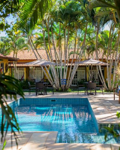 a swimming pool with tables and umbrellas and palm trees at Villa Bella Ferradura in Búzios
