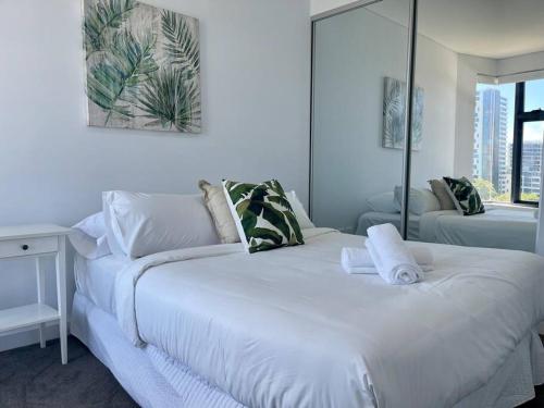 a white bedroom with a large bed with towels on it at Cosy Stays 1 Bedroom Apartment Rosebery Parking & Balcony Sydney Escape in Sydney