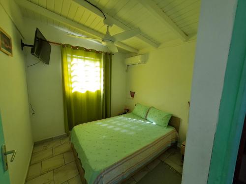 ein kleines Schlafzimmer mit einem grünen Bett und einem Fenster in der Unterkunft O 4 épices gites in Capesterre-Belle-Eau