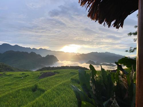 a view of a green field with the sun setting over mountains at Pu Luong Ecocharm in Hương Bá Thước