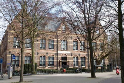 un grand bâtiment en briques avec des arbres devant lui dans l'établissement The College Hotel Amsterdam, Autograph Collection, à Amsterdam
