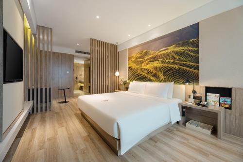 - une chambre avec un grand lit blanc et un tableau dans l'établissement Atour Hotel Nanning Nanhu Subway Station, à Nanning