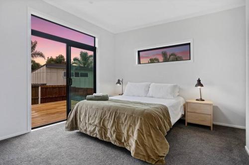 a white bedroom with a bed and a large window at Another on Leo in Waihi Beach