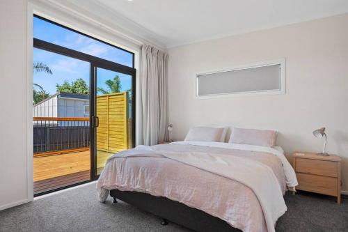 a white bedroom with a bed and a balcony at Leisure on Leo in Waihi Beach