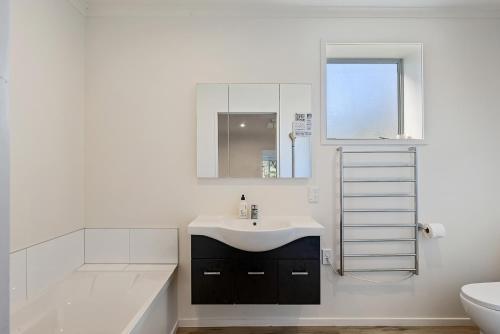 a white bathroom with a sink and a bath tub at Beachfront Favourite - Foxton Beach Holiday Home in Foxton Beach