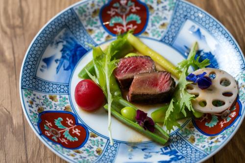 a blue and white plate of food with meat and vegetables at 宿坊　心月 in Arita