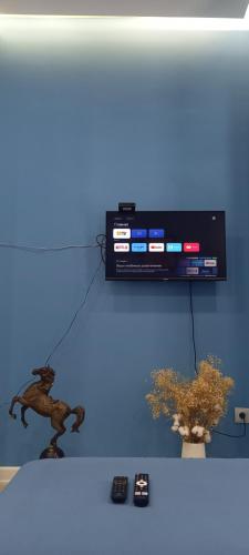 a television on a blue wall with two remote controls at Aylin apartments 359/3 in Almaty