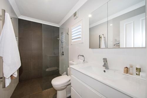 a white bathroom with a toilet and a sink at Woy Woy Staycation - Heated Pool & Hot Tub & BBQ & Pizza Oven & Arcade Game & Pool Table in Woy Woy