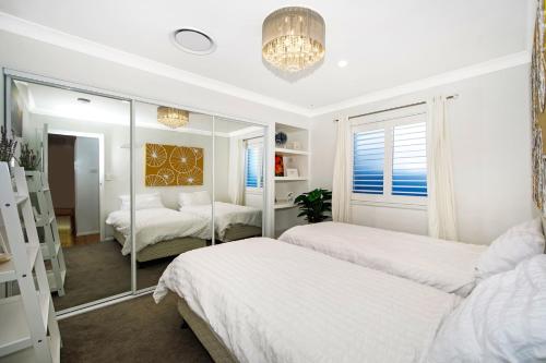 a white bedroom with two beds and a mirror at Woy Woy Staycation - Luxury Pool & Spa & Games Vacation in Woy Woy