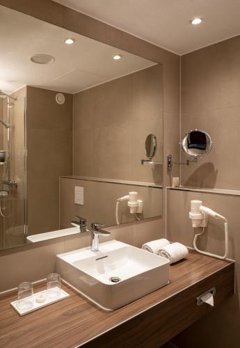a bathroom with a sink and a large mirror at H+ Hotel Hannover in Hannover