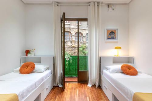two beds with orange pillows in a room with a window at INAR céntrico apartamento junto Ayuntamiento & Ría in Bilbao