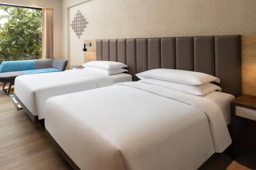 two white beds in a room with a chair at Hyatt Place Vijayawada in Vijayawāda
