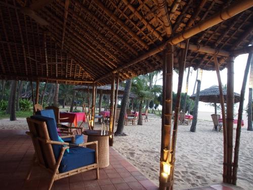 a patio with chairs and tables on a beach at Neeleshwar Hermitage in Nīleshwar