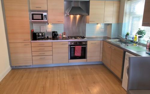 uma cozinha com armários de madeira e electrodomésticos de aço inoxidável em Addlestone - Stylish and modern 2 bedroom apartment em Addlestone