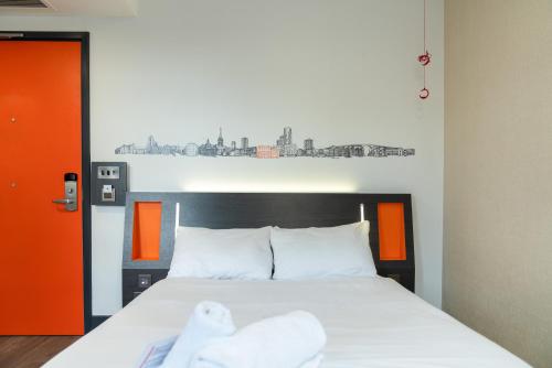 a bedroom with a white bed with an orange wall at easyHotel Ipswich in Ipswich