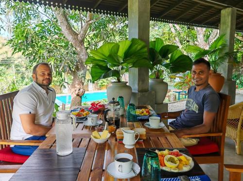two men sitting at a wooden table with food on it at Villa Lyvie ayurvedic hotel in Tangalle