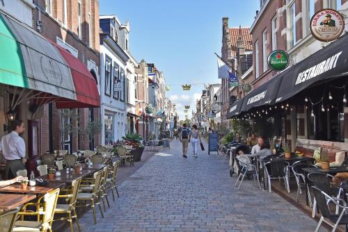 een straat met tafels en stoelen en mensen die over straat lopen bij Four Star Apartments - Keizerstraat in Scheveningen