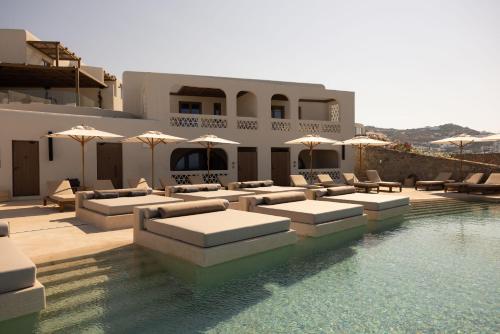 una piscina con sofás y sombrillas junto a una casa en Domes Noruz Mykonos en Mykonos