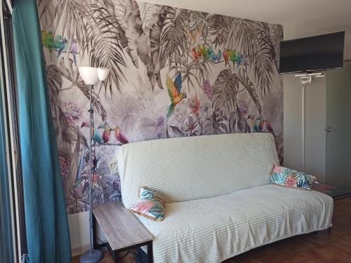 een woonkamer met een witte bank en tropisch behang bij Appartement centre port Cap d'Agde in Cap d'Agde