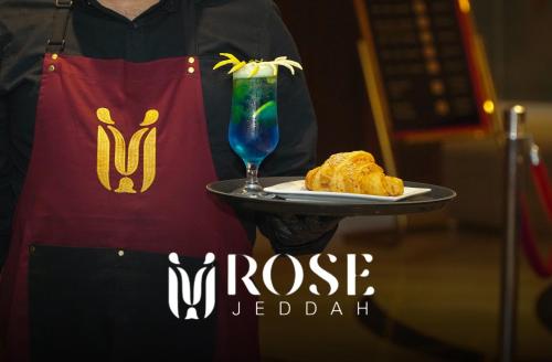 uma pessoa segurando uma bandeja com uma bebida e um prato de comida em Rose Jeddah Hotel em Jidá