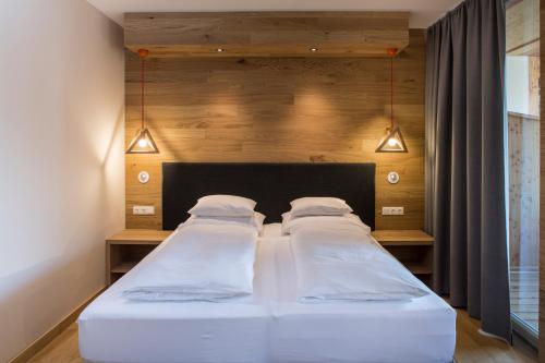two beds in a bedroom with a headboard and lights at Falkensteiner Aktiv & Familienhotel Cristallo in Katschberghöhe