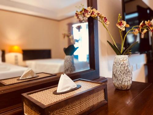 a table with a mirror and a vase with flowers at Na Thapae Chiangmai Hotel in Chiang Mai