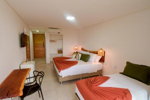 a bedroom with two beds and a table and a desk at Milie Lounge Pousada in Japaratinga
