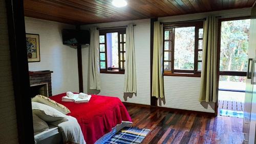 a bedroom with a bed with a red blanket and windows at Pousada Bosque do Visconde in Visconde De Maua