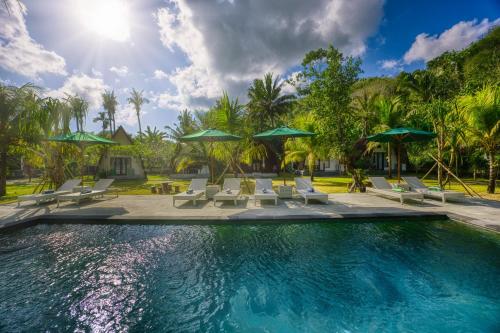 a swimming pool with chairs and umbrellas at Puri Garden Penida in Nusa Penida