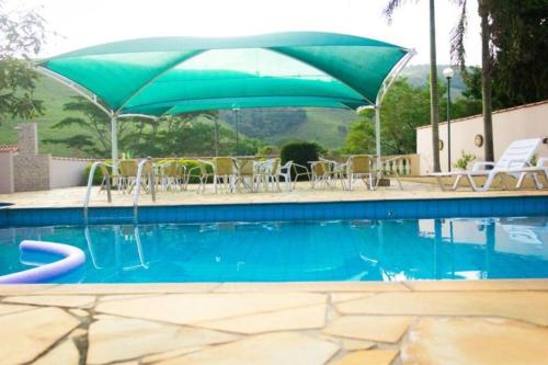 a swimming pool with a green umbrella and chairs at Recanto dos Beija flores, Chalé Lantana c in Monte Alegre do Sul