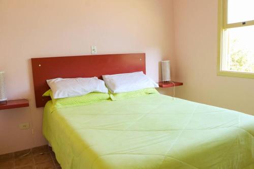 um quarto com uma cama grande com lençóis e almofadas verdes em Recanto dos Beija flores, Chalé Lantana c em Monte Alegre do Sul