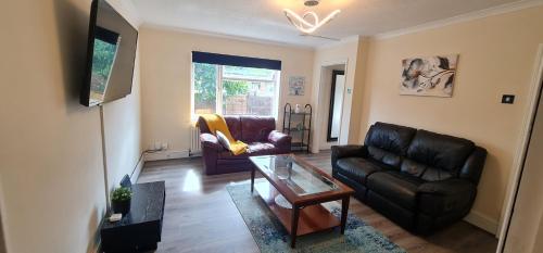 a living room with a leather couch and a glass table at 6 Bedroom Spacious villa, Free Parking in Byfleet
