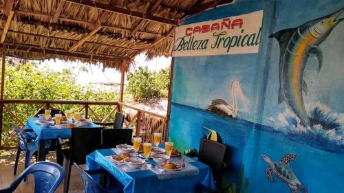 un restaurant avec des tables bleues et un panneau indiquant la cuisine tropicale de l'océan dans l'établissement HOSTAL BELLEZA TROPICAL, à Moñitos