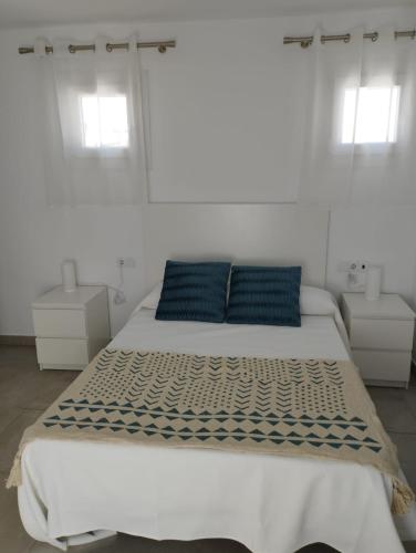 a white bedroom with a large bed with blue pillows at APARTAMENTOS TRES SOLES in Écija