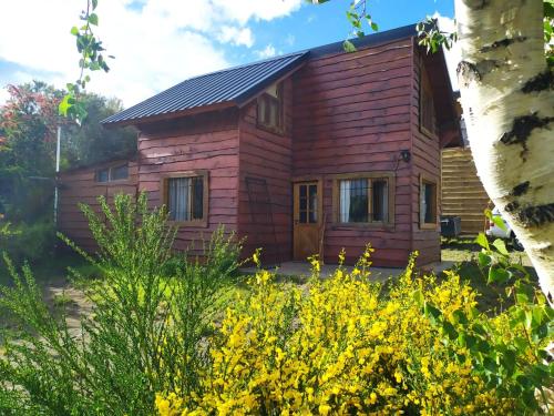a wooden house with yellow flowers in front of it at Cabañas Boca del Chimehuín in Junín de los Andes