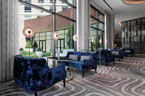 a lobby with blue chairs and tables and windows at Le Meridien Pasadena Arcadia in Arcadia