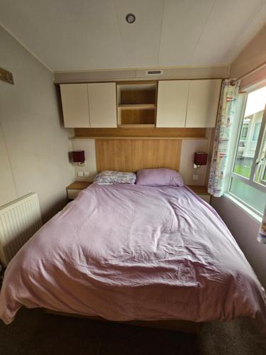 Caravan 4 - Cambrian Coast Caravan Park في بورث: غرفة نوم مع سرير كبير مع ملاءات أرجوانية