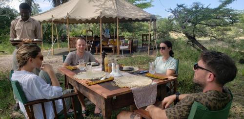 Kwa Mhinda的住宿－Makubi Safari Camp by Isyankisu，一群人坐在木桌旁