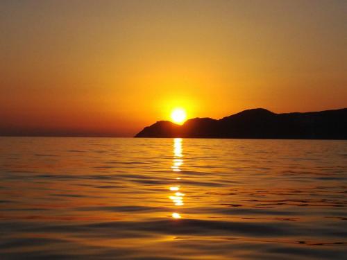 a sunset over the water with mountains in the background at Tholos Alexandra's Beachfront House in Kavoúsion