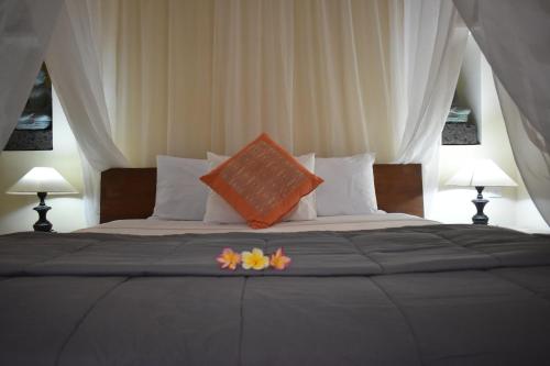 un letto con un cuscino arancione e fiori sopra di Umah Ubud B&B ad Ubud