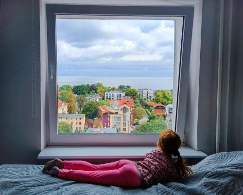 a little girl laying on a bed looking out a window at Pokoje przy plaży z widokiem na morze in Sopot