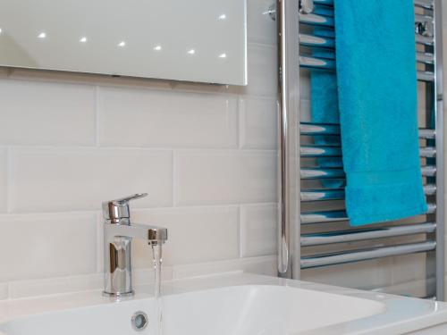 ein Badezimmer mit einem Waschbecken, einem Spiegel und blauen Handtüchern in der Unterkunft Harewood Barn in Brompton Regis